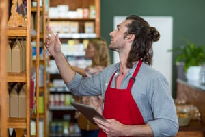 Male staff holding a digital tablet and checking grocery products on the shelf in supermarket