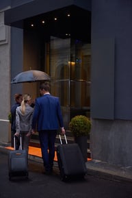 Young business people couple entering city  hotel, looking for room, holding suitcases while walking on street